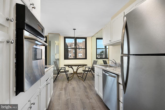 kitchen with white cabinets, appliances with stainless steel finishes, wood finished floors, light countertops, and a sink