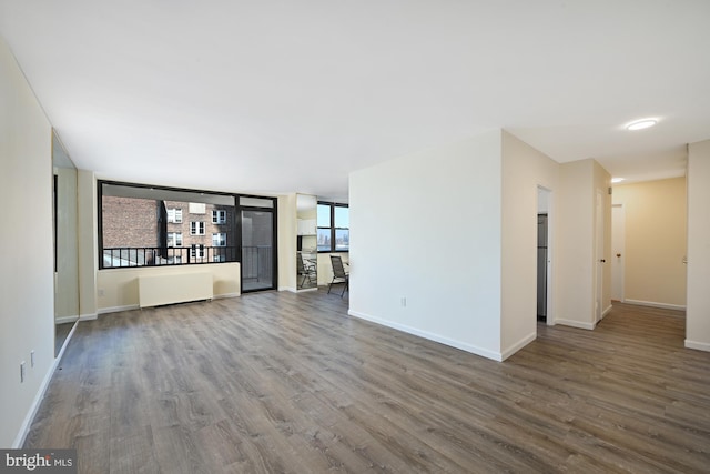 unfurnished living room featuring radiator heating unit, wood finished floors, and baseboards