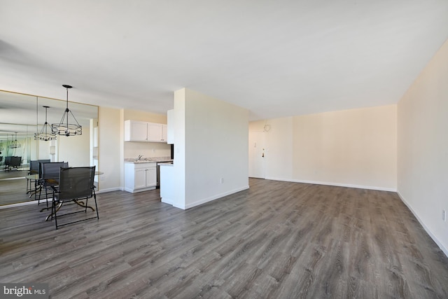 unfurnished living room with dark wood-style floors, a chandelier, and baseboards