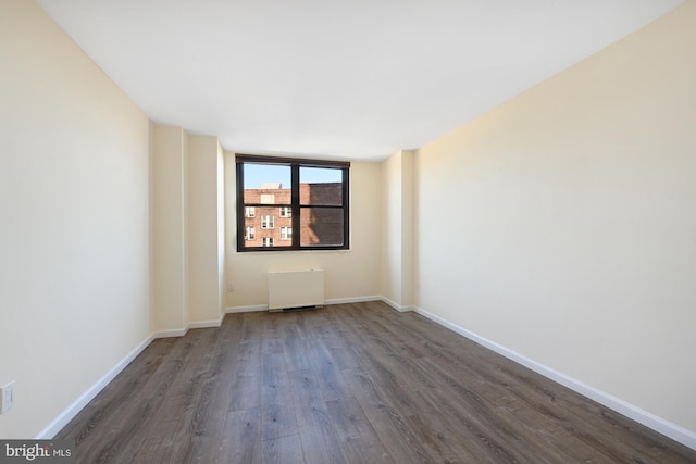 empty room with baseboards, dark wood-style flooring, and radiator