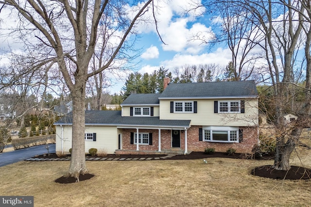 traditional home with brick siding, a shingled roof, driveway, a front lawn, and a chimney