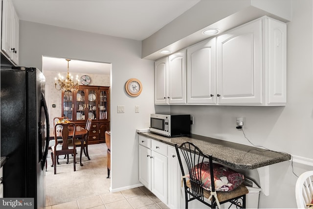 kitchen featuring stainless steel microwave, dark countertops, white cabinetry, freestanding refrigerator, and an inviting chandelier