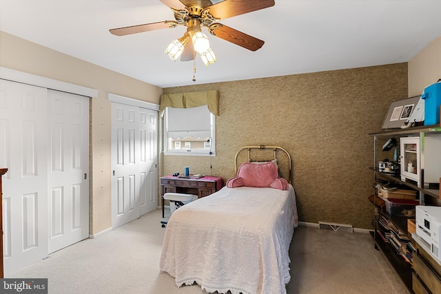 carpeted bedroom with visible vents, wallpapered walls, two closets, baseboards, and a ceiling fan