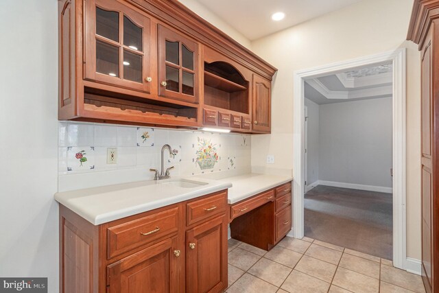 kitchen with light tile patterned floors, a sink, glass insert cabinets, a raised ceiling, and tasteful backsplash