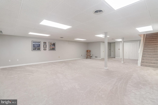 finished below grade area with light carpet, visible vents, stairs, and baseboards