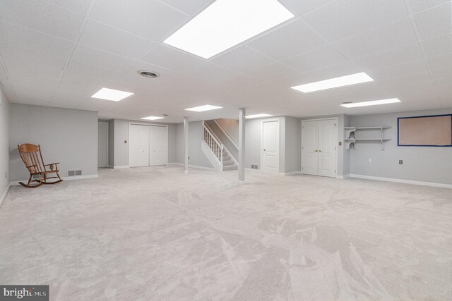 finished basement with a drop ceiling, visible vents, and stairs