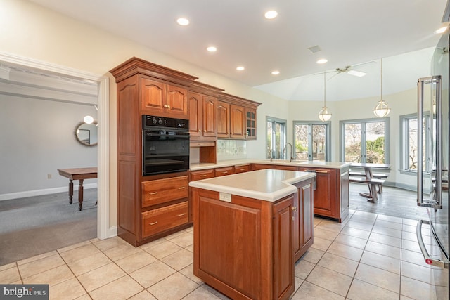 kitchen featuring black oven, a peninsula, brown cabinetry, and light countertops