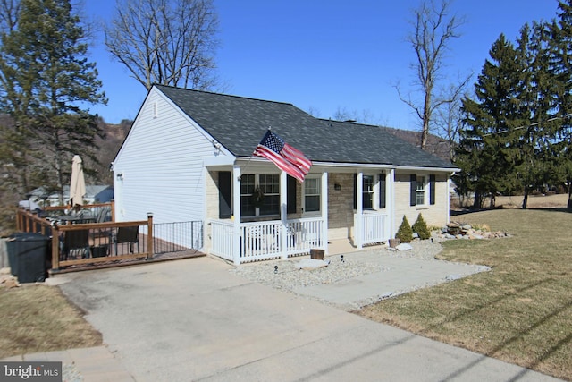 view of front of house featuring a porch, concrete driveway, a front yard, and a shingled roof