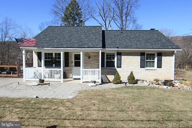 view of front facade featuring covered porch, a shingled roof, a front yard, and brick siding