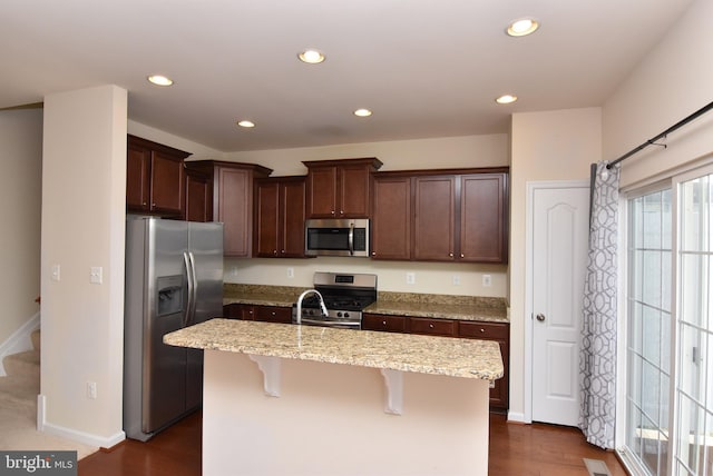 kitchen featuring dark brown cabinetry, an island with sink, light stone counters, recessed lighting, and appliances with stainless steel finishes