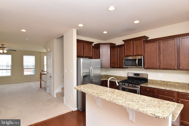 kitchen featuring a kitchen island with sink, light stone counters, recessed lighting, appliances with stainless steel finishes, and a breakfast bar area