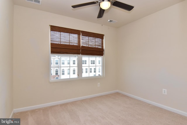 spare room featuring light carpet, visible vents, ceiling fan, and baseboards