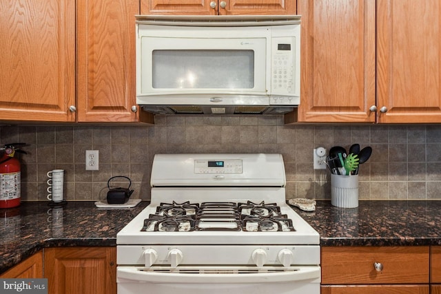 kitchen featuring dark stone countertops, white appliances, backsplash, and brown cabinets