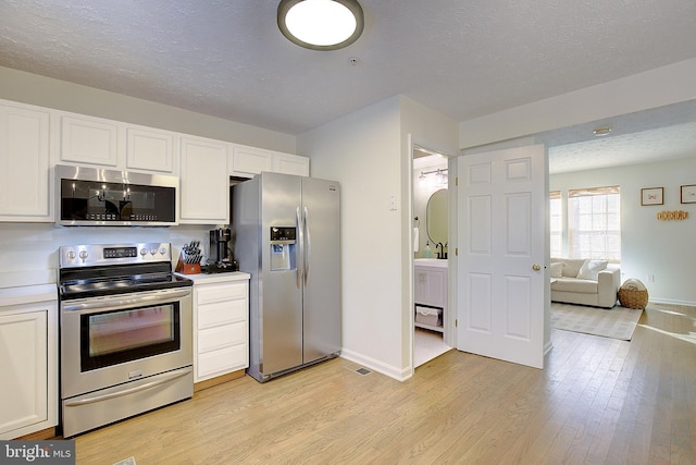 kitchen with white cabinetry, light wood-style flooring, appliances with stainless steel finishes, and a textured ceiling