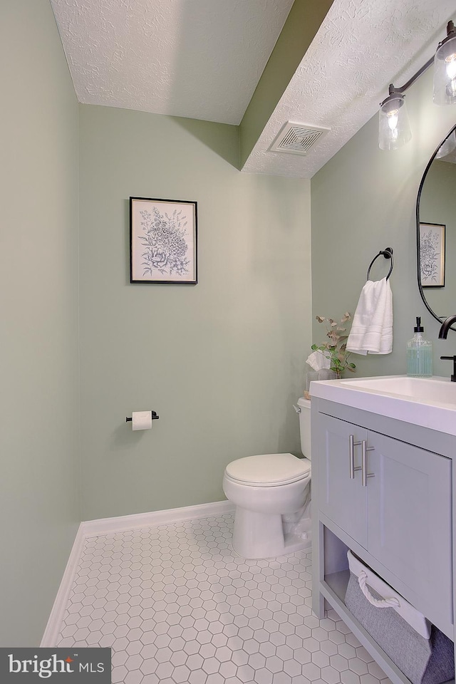 half bath with a textured ceiling, tile patterned flooring, toilet, vanity, and visible vents