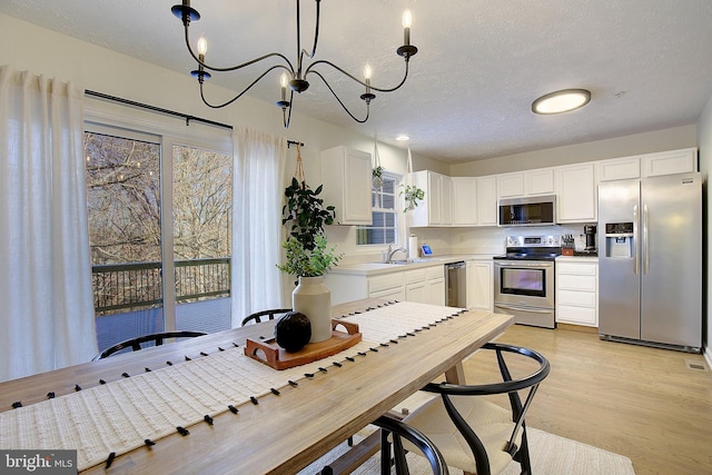 kitchen with a textured ceiling, a sink, white cabinets, appliances with stainless steel finishes, and light wood finished floors