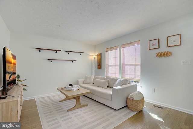 living area with light wood-style floors, baseboards, visible vents, and a textured ceiling