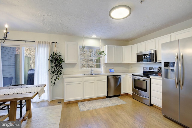 kitchen with stainless steel appliances, light countertops, light wood-style floors, white cabinets, and a sink