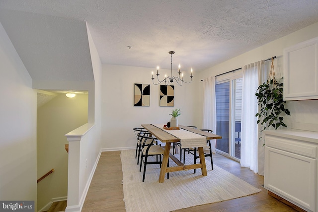 dining space with light wood-style floors, baseboards, a textured ceiling, and an inviting chandelier