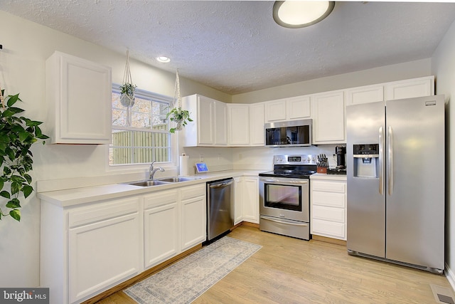 kitchen with stainless steel appliances, a sink, white cabinetry, light wood-style floors, and light countertops