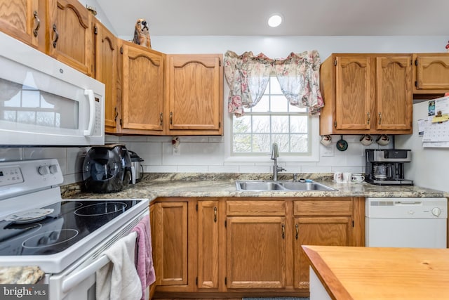 kitchen with white appliances, brown cabinetry, backsplash, and a sink