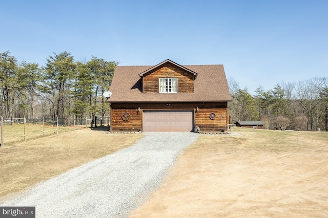 chalet / cabin with gravel driveway, fence, a garage, and roof with shingles