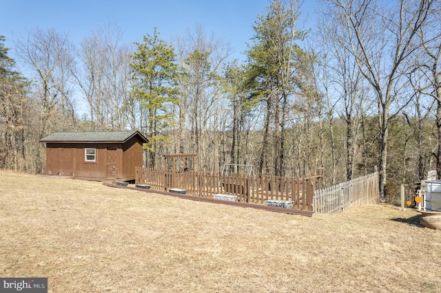 view of yard featuring an outbuilding, a wooden deck, a forest view, and fence