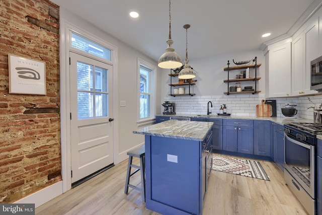 kitchen with light wood finished floors, open shelves, stainless steel appliances, a sink, and blue cabinets