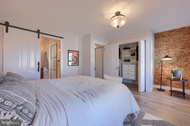 bedroom featuring a closet, a barn door, light wood-style floors, brick wall, and baseboards