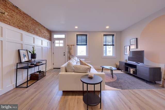 living area with arched walkways, light wood finished floors, a decorative wall, and recessed lighting