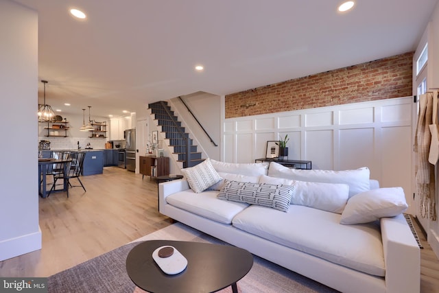 living area featuring stairs, brick wall, light wood finished floors, and recessed lighting