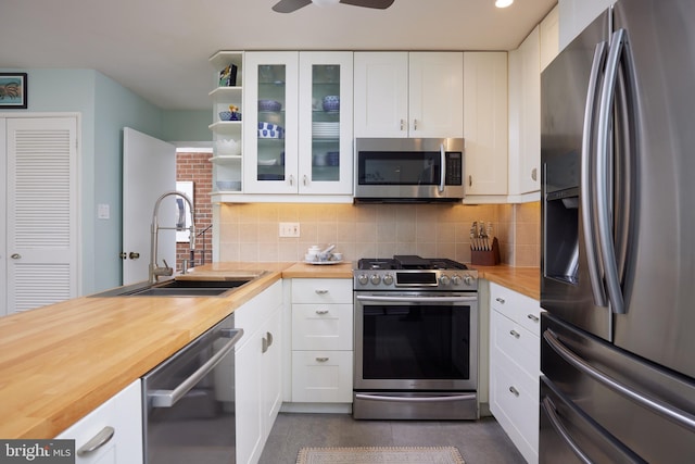 kitchen featuring open shelves, a sink, stainless steel appliances, wood counters, and backsplash