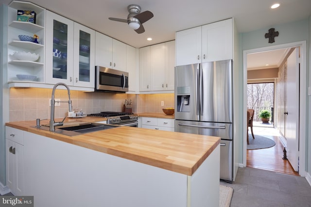 kitchen with butcher block counters, a peninsula, stainless steel appliances, white cabinetry, and a sink