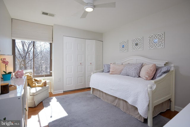 bedroom with a ceiling fan, wood finished floors, visible vents, baseboards, and a closet