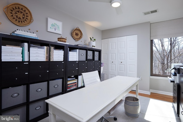 office area with light wood finished floors, visible vents, baseboards, and a ceiling fan