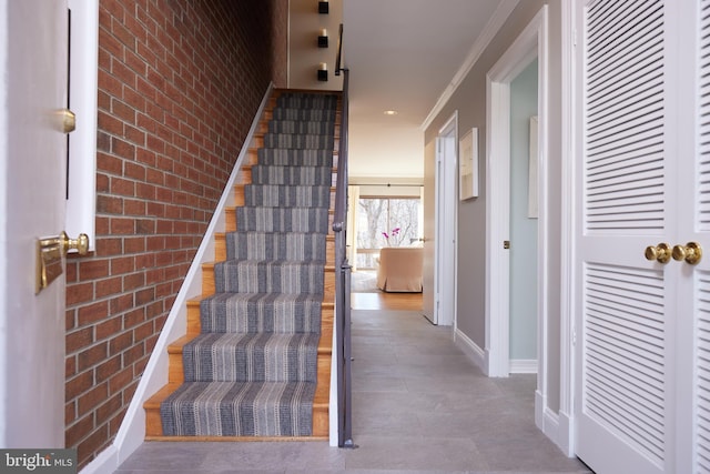 staircase with baseboards, brick wall, an accent wall, and crown molding