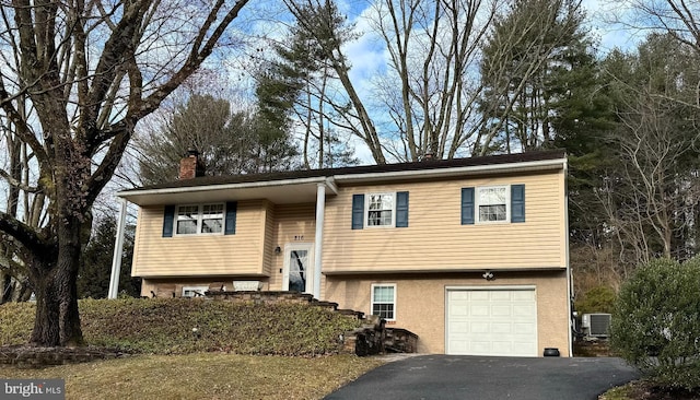 raised ranch with stucco siding, cooling unit, a chimney, a garage, and driveway