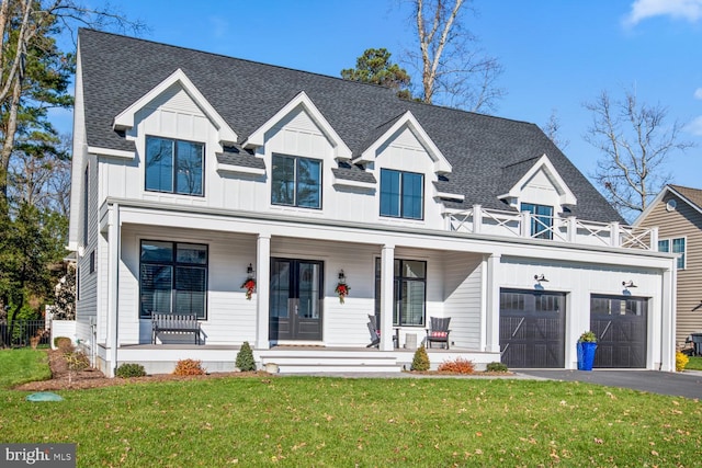 modern inspired farmhouse with aphalt driveway, covered porch, a garage, roof with shingles, and a front yard