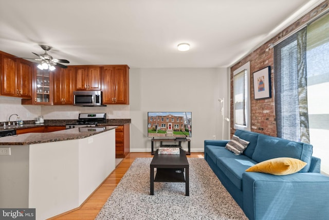 kitchen featuring glass insert cabinets, appliances with stainless steel finishes, brown cabinets, dark stone countertops, and light wood-type flooring