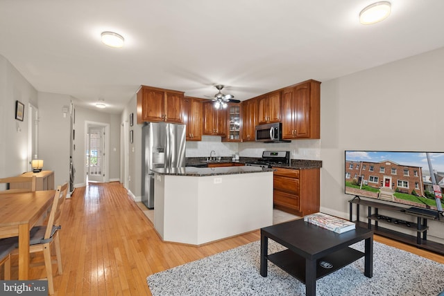 kitchen with a kitchen island, appliances with stainless steel finishes, brown cabinets, light wood finished floors, and glass insert cabinets