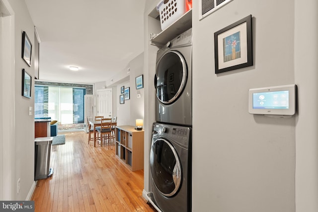 clothes washing area featuring baseboards, laundry area, light wood-style flooring, and stacked washer / drying machine