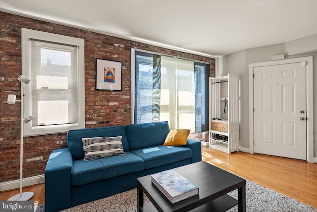 living area with baseboards, light wood-style flooring, and brick wall