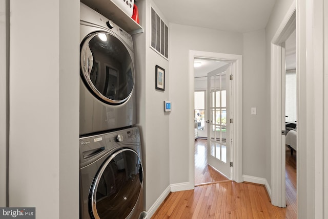 washroom featuring stacked washer and dryer, laundry area, visible vents, baseboards, and light wood-style flooring