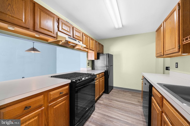 kitchen featuring brown cabinets, under cabinet range hood, light countertops, light wood-type flooring, and black appliances