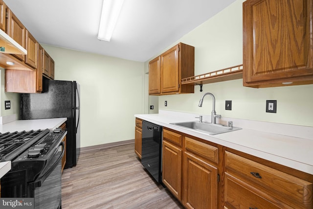 kitchen featuring brown cabinetry, light wood-style flooring, light countertops, black appliances, and a sink