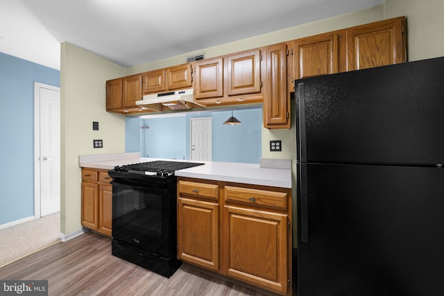 kitchen featuring light countertops, light wood-style flooring, brown cabinetry, under cabinet range hood, and black appliances