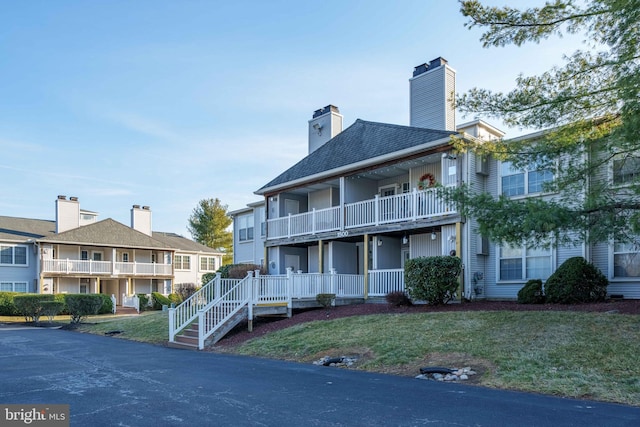 exterior space with a balcony, a chimney, a front lawn, and a porch