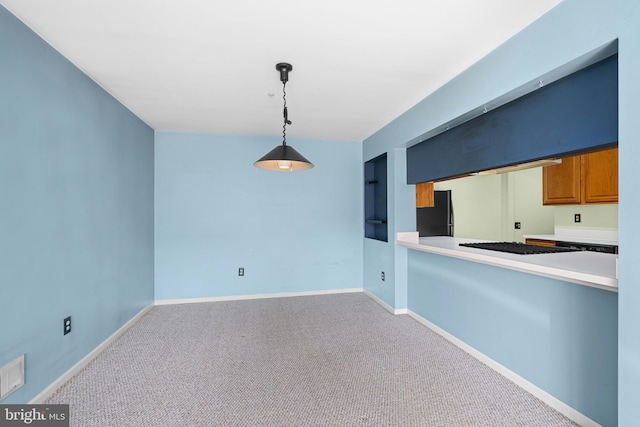 kitchen featuring carpet, hanging light fixtures, brown cabinetry, freestanding refrigerator, and baseboards