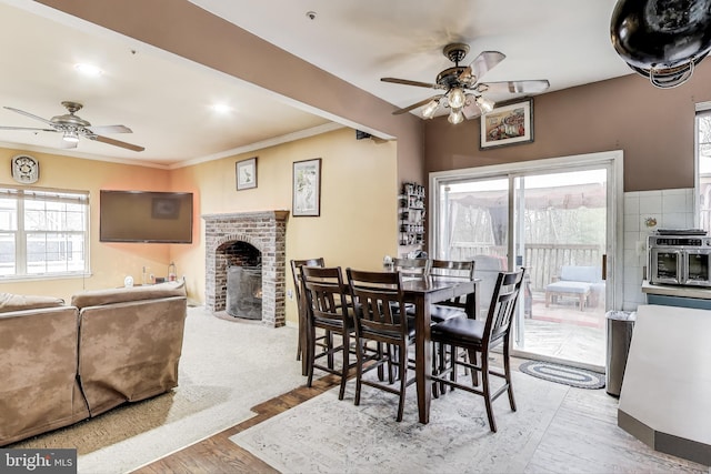 dining space with wood finished floors, a brick fireplace, ornamental molding, and a ceiling fan