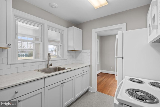 kitchen featuring tasteful backsplash, white cabinets, a sink, white appliances, and baseboards